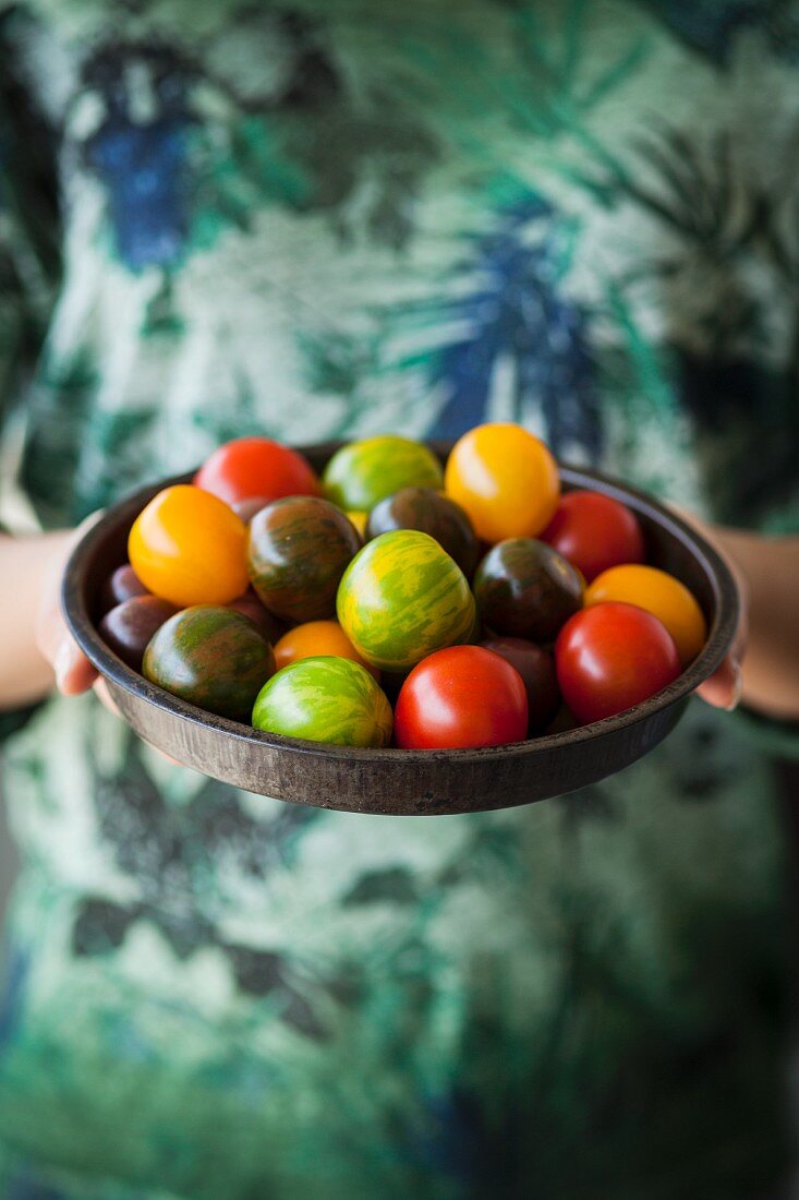A woman holding a dish of different-coloured tomatoes