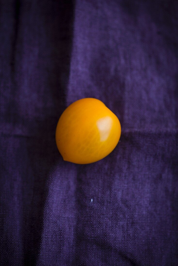 A yellow tomato on a violet cloth