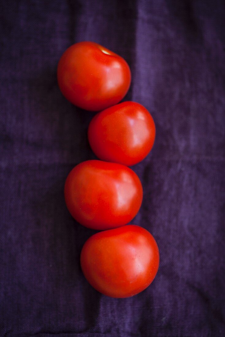 Vier rote Tomaten auf violettem Tuch