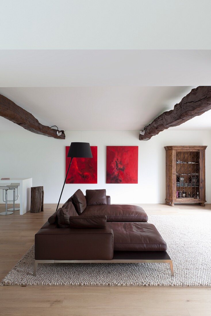 Dark brown leather couch and rustic ceiling beams in open-plan living area