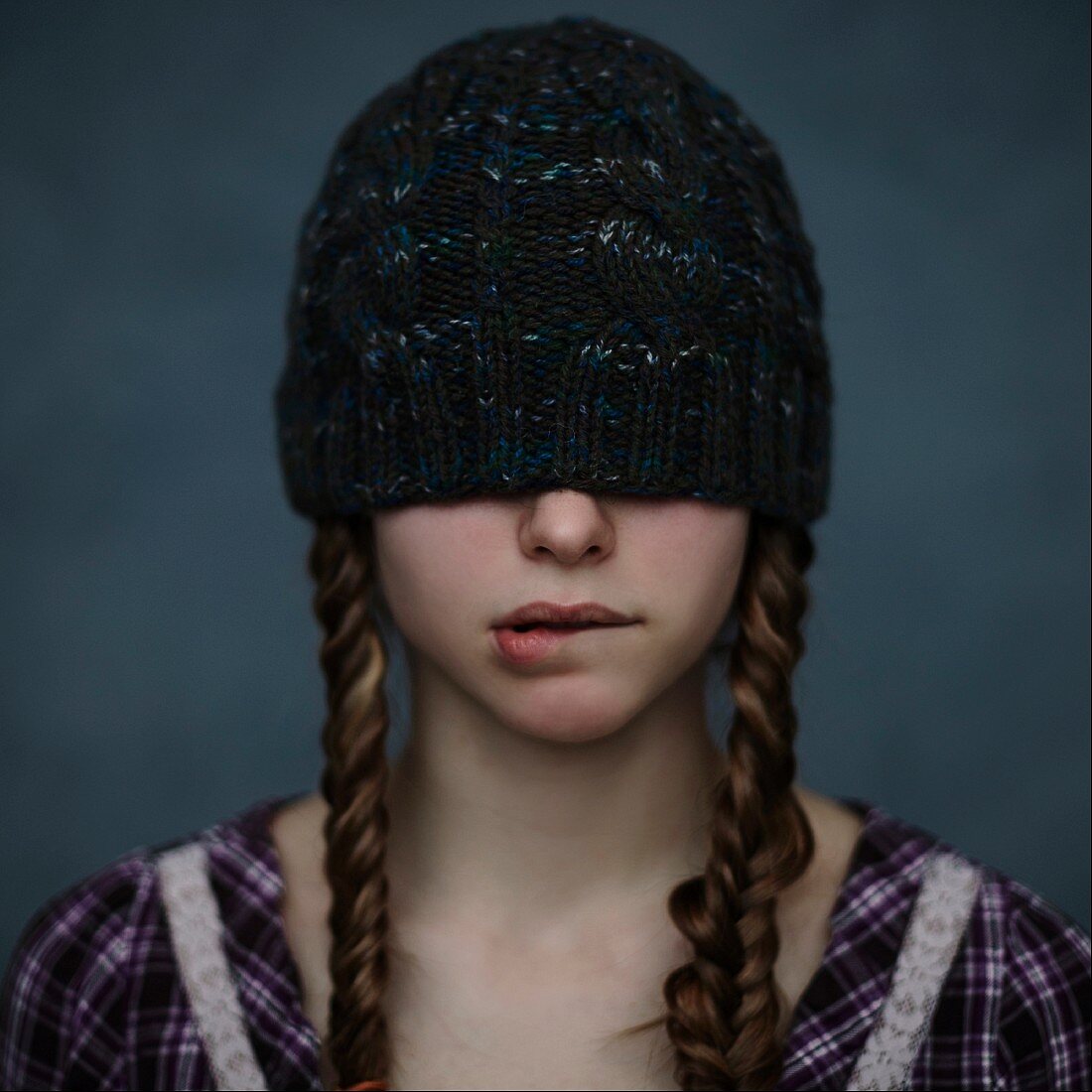 A girl with her hair in two plaits and with a knitted beanie hat over eyes