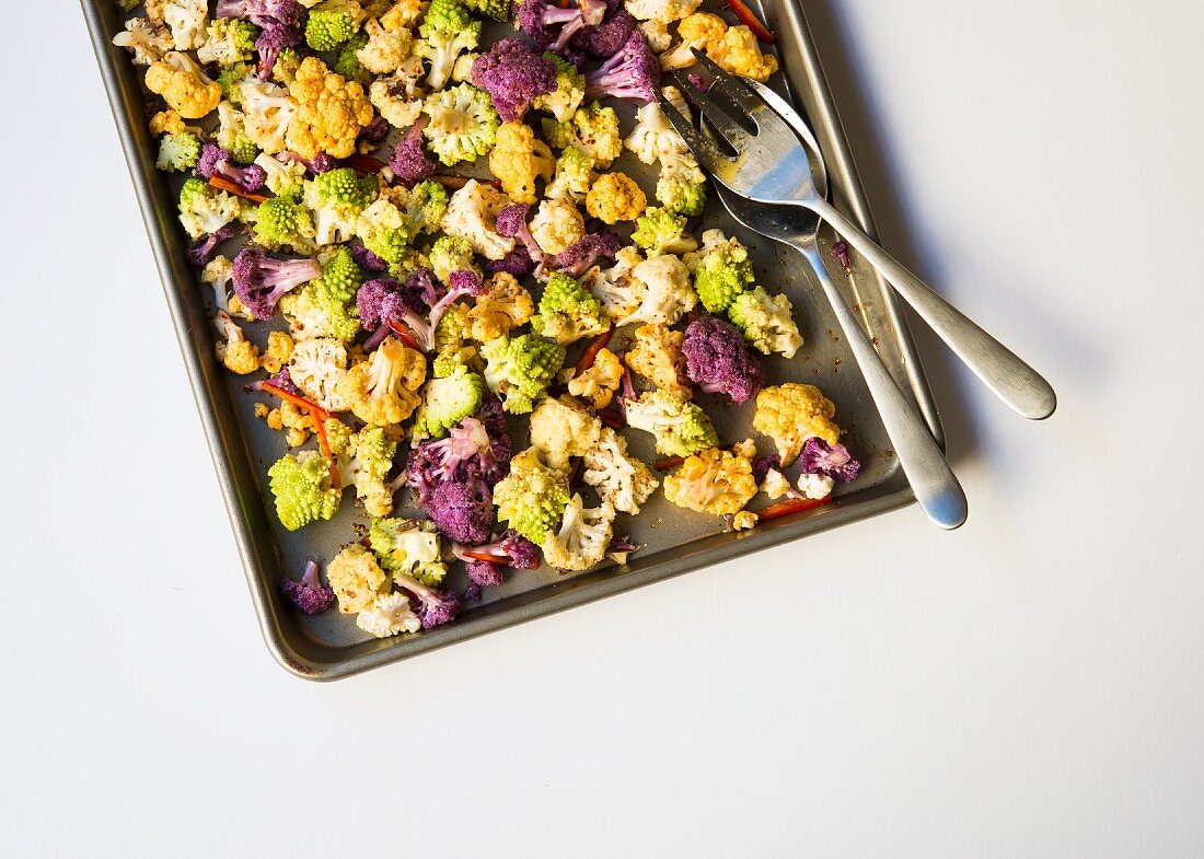 Florets of Romanesco, white cauliflower and purple cauliflower on a baking tray ready to be roasted