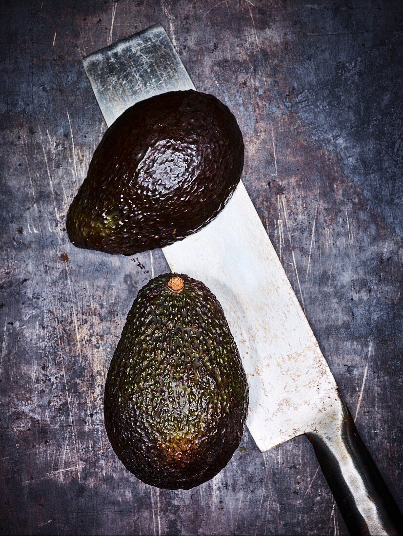 An avocado cut in half with a knife on a grey background (seen from above)