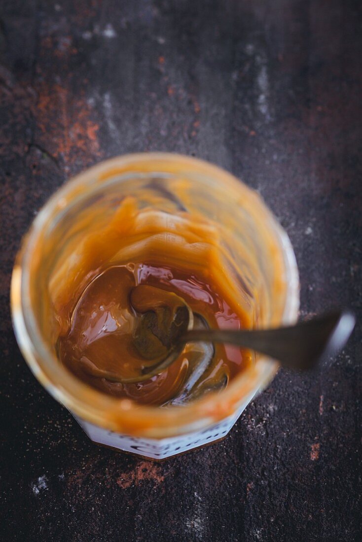 Leftover caramel sauce in a glass jar with a spoon