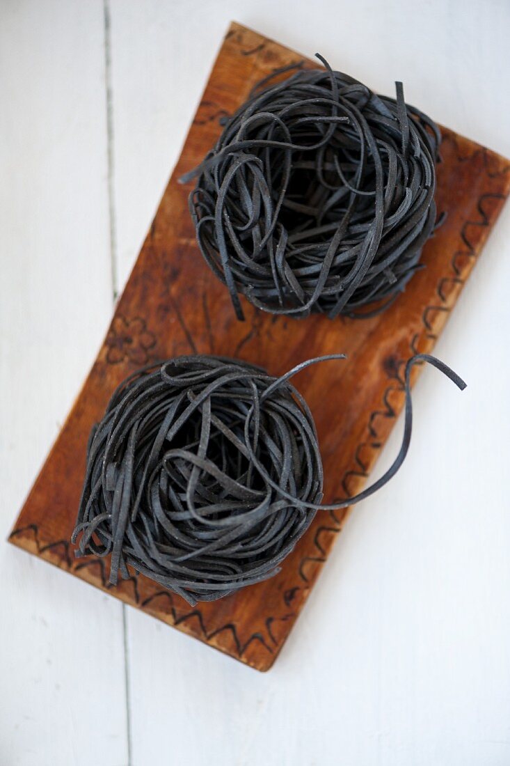 Zwei Nudelnester aus schwarzen Sepianudeln auf Holzbrett