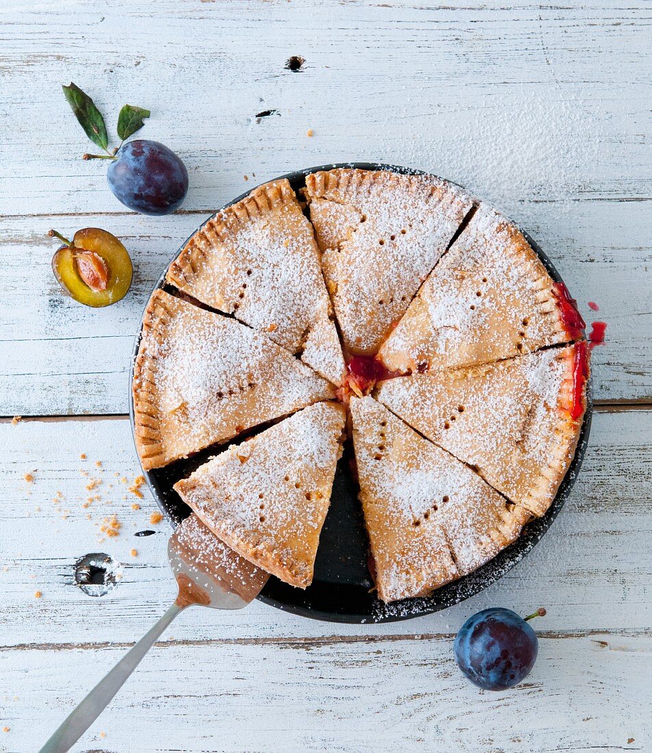 A sliced plum pie dusted with icing sugar