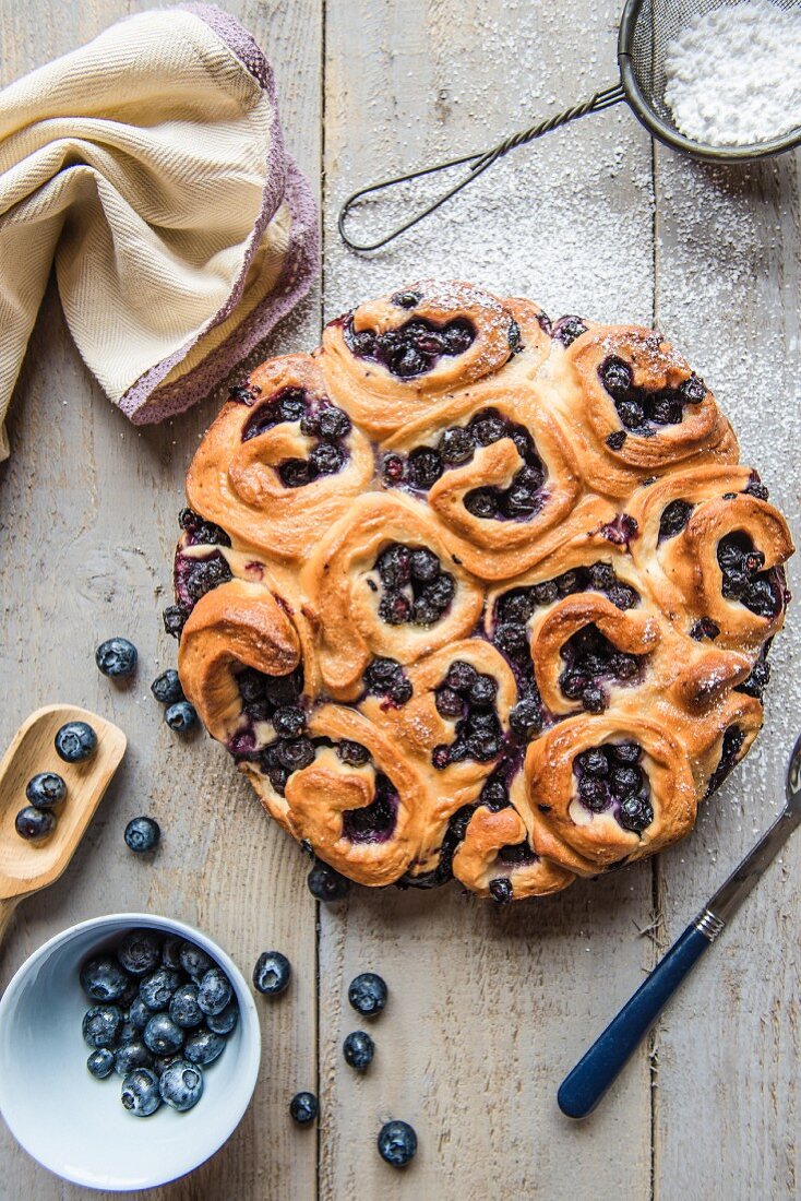 A crown of sweet yeast buns with blueberries and icing sugar (seen from above)