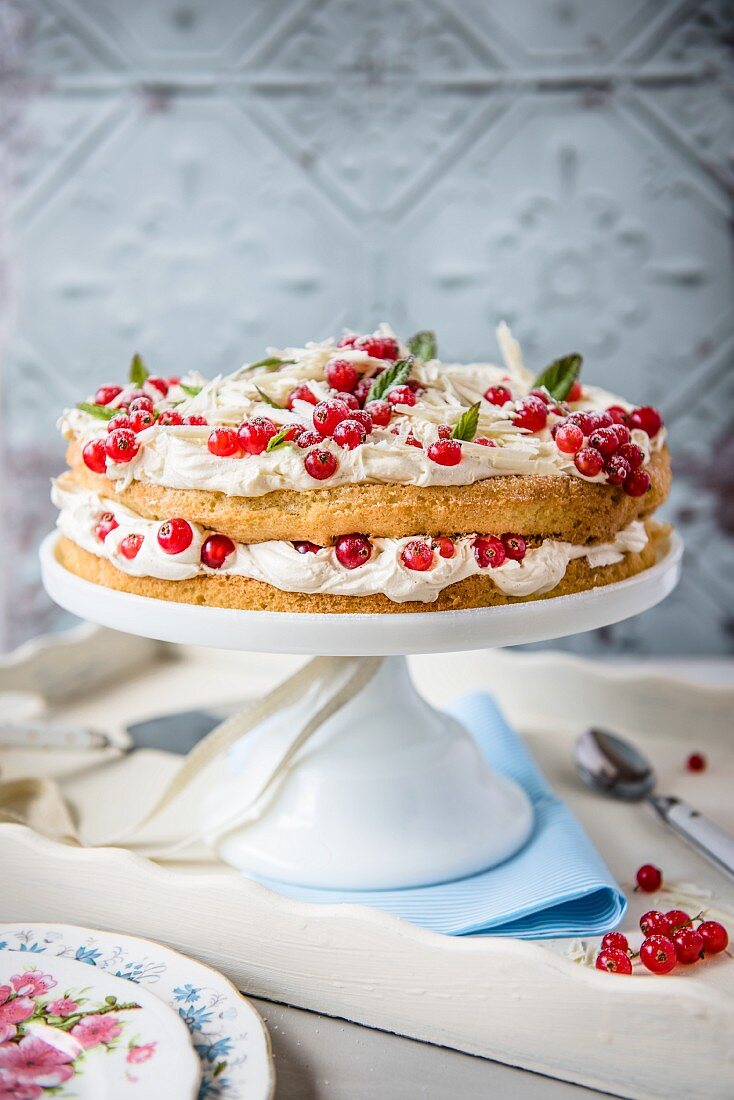 A cake with white chocolate cream and redcurrants on a cake stand
