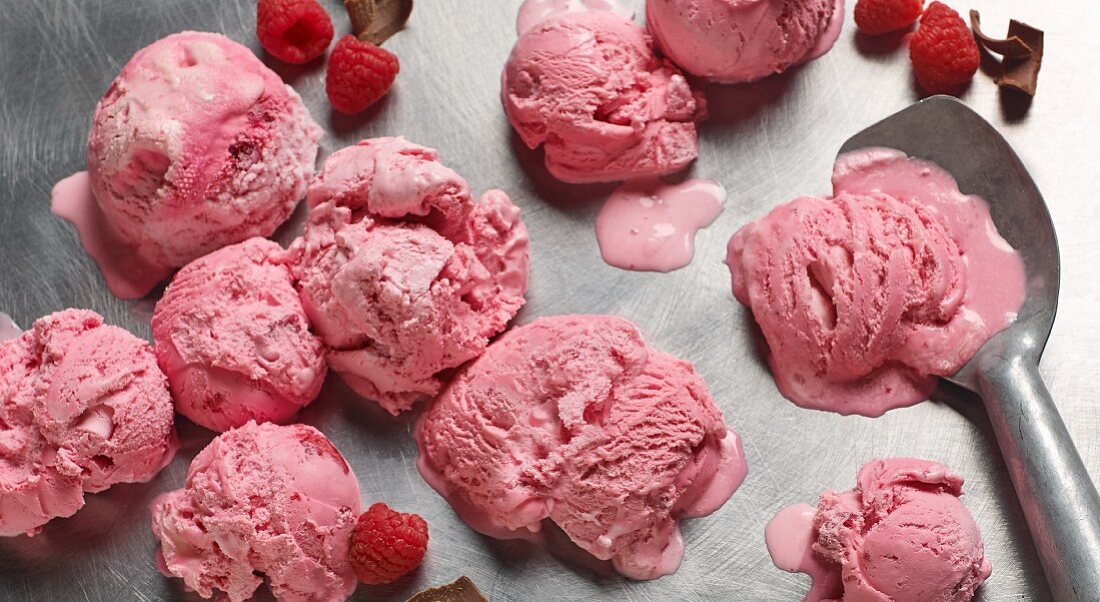 Raspberry ice cream with an ice cream scoop on a metal surface