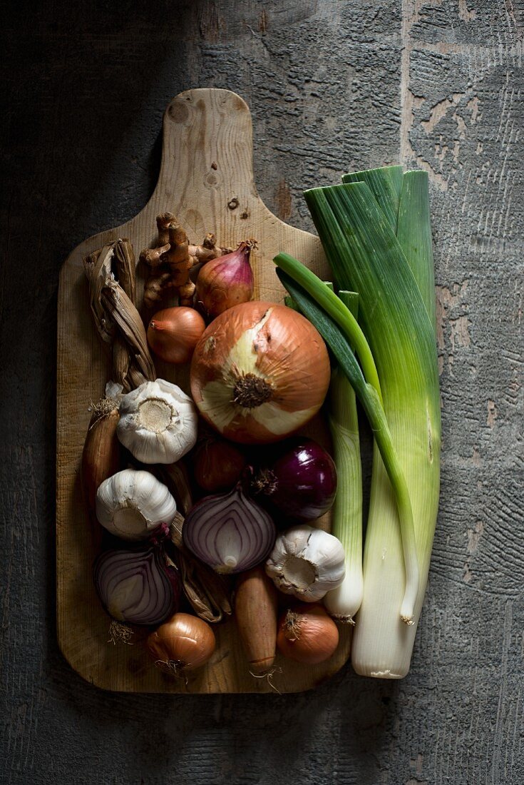 An arrangement of onions, garlic and leeks on a chopping board (seen from above)
