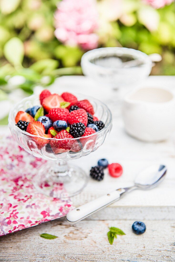A summer berry salad with mint in a glass bowl on a garden table