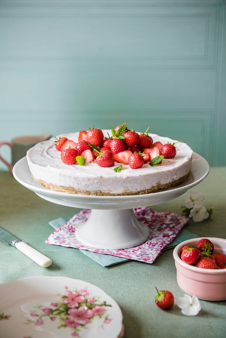 Strawberry cheesecake on a cake stand with fresh strawberries and mint