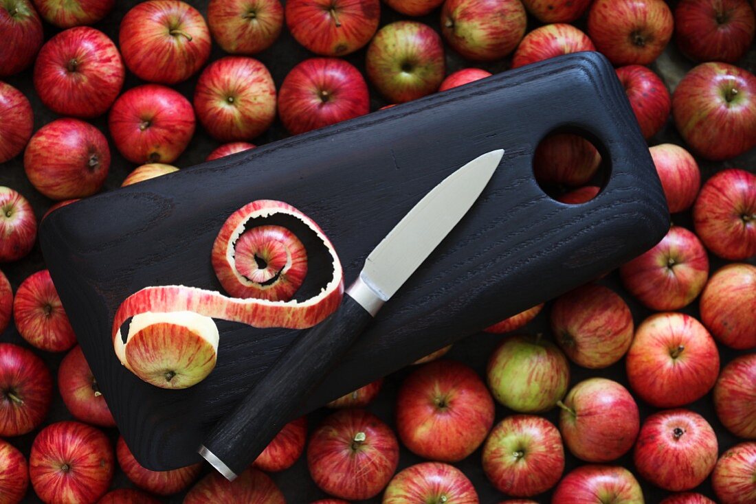 A wooden chopping board with a knife on red apples