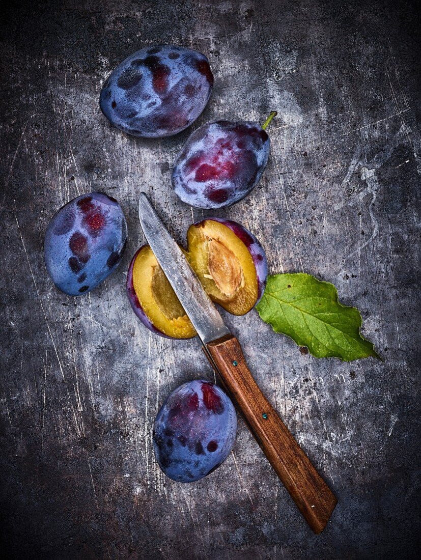 Whole and halved plums with a knife on a metal surface