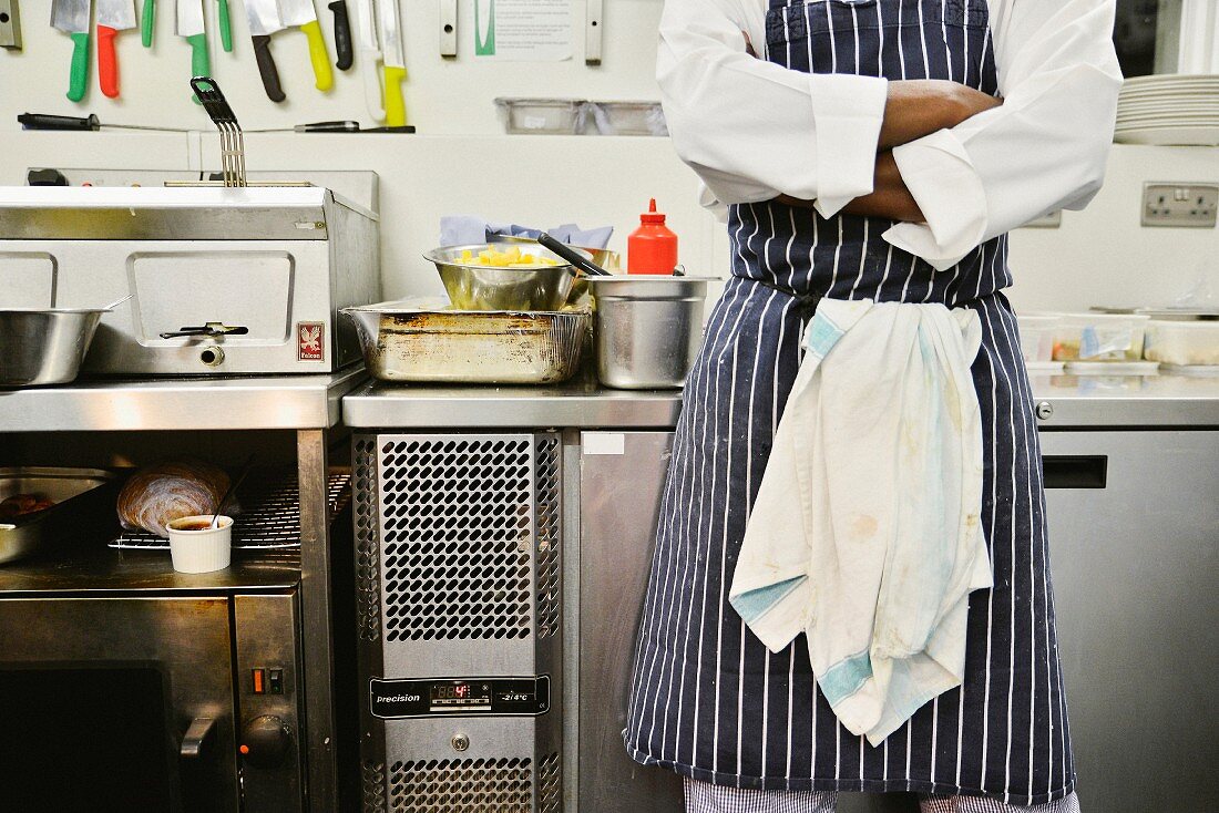 A chef standing in a commercial kitchen with his arms folded