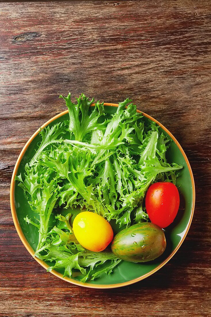 Fresh green salad leaves with colourful tomatoes (seen from above)