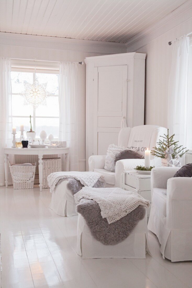 Two armchairs with footstools in front of corner cabinet in corner of white living room