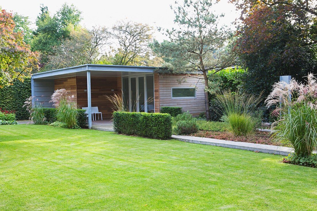 Well-tended lawn in garden outside flat-roofed building with roofed terrace