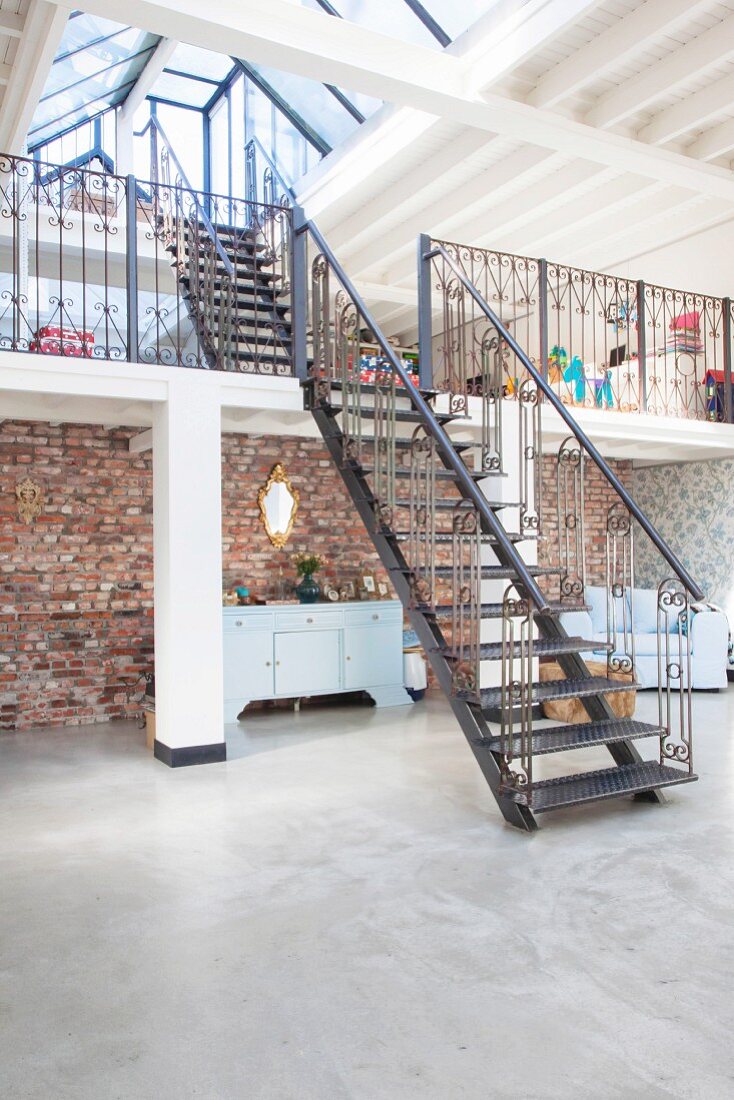Stahltreppen zu zwei Galerieebenen in Loft mit Betonboden und rustikaler Ziegelwand