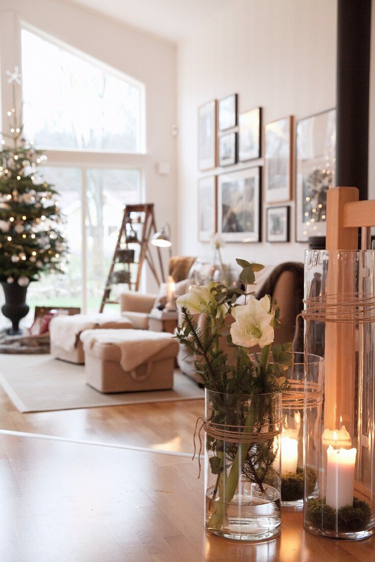 Glass vase of hellebores, candle lanterns on wooden floor and decorated Christmas tree in lounge area in background