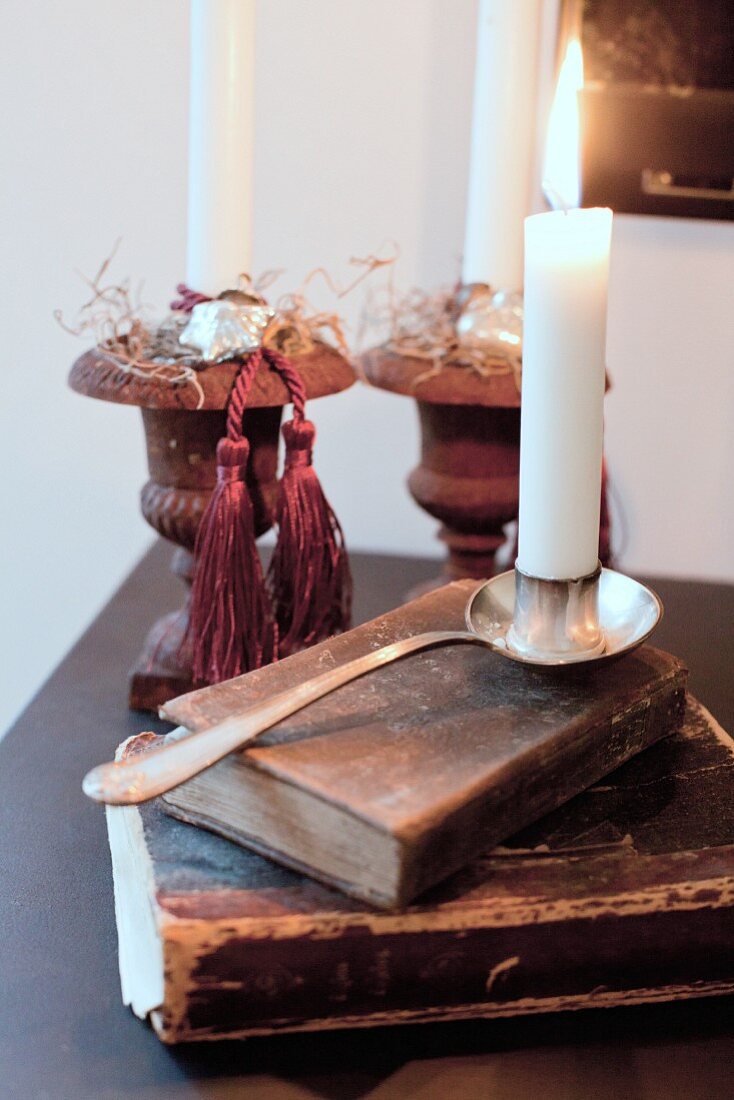 Silberner Kerzenhalter mit brennender Kerze auf antiquarischem Buch