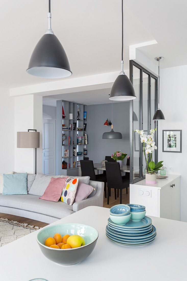 Crockery stacked on white worksurface, partition wall, couch and dining area in background