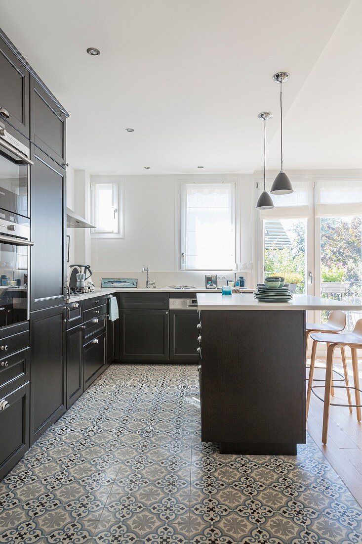 Black fitted kitchen with white worksurface and ornamental tiled floor