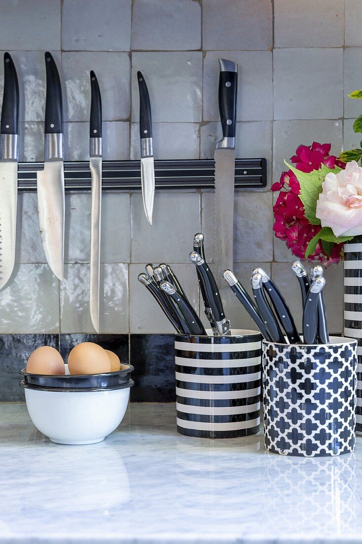 Several kitchen knives on magnetic strip in kitchen with white marble worksurface