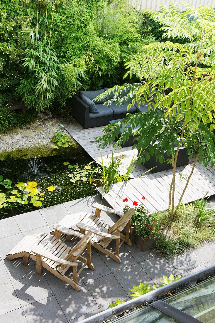 Garden pond, wooden lounger and sofa on wooden deck next to bamboo
