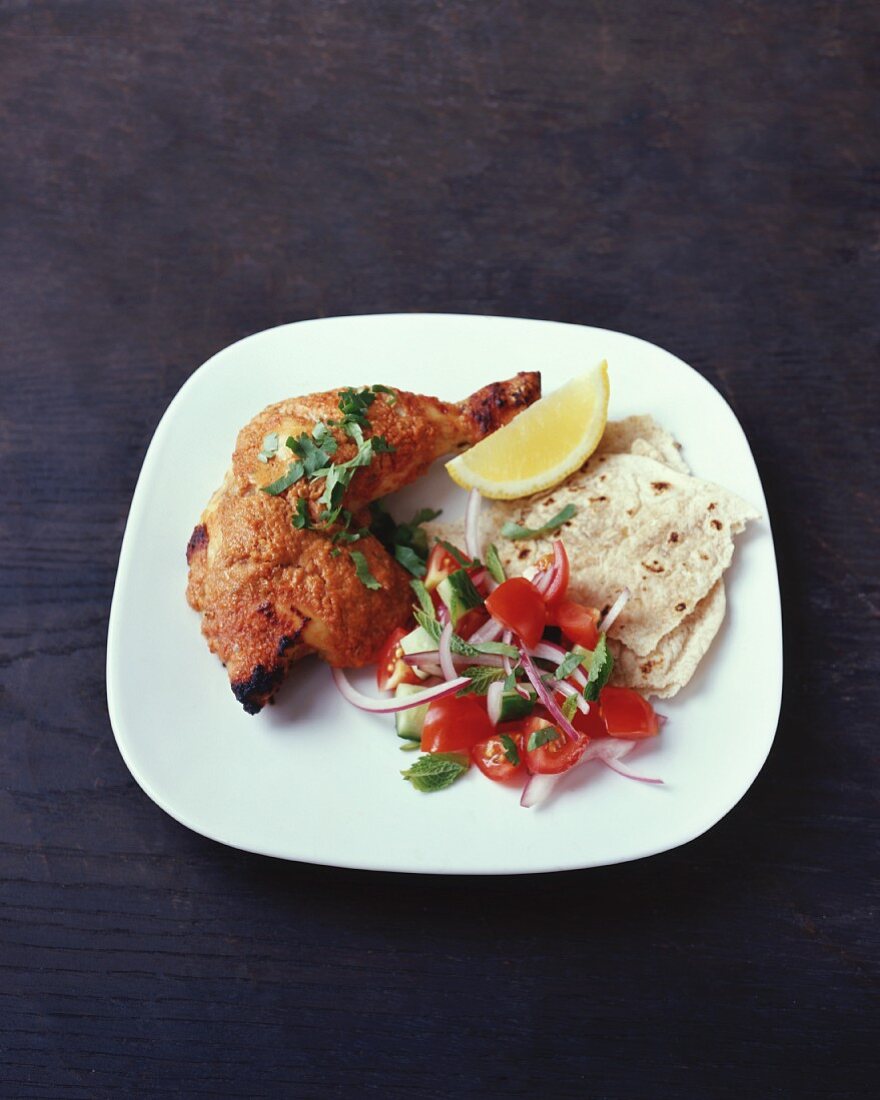 A chicken drumstick with tomato salad and flatbread