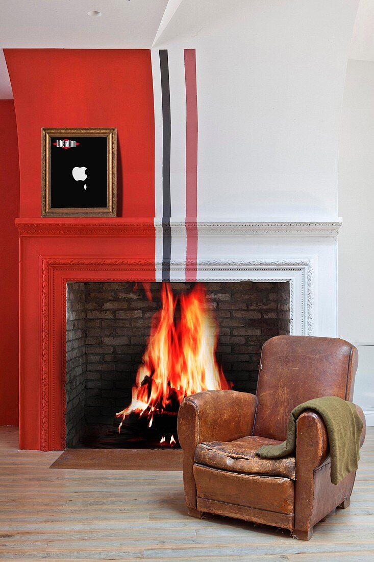 Vintage leather armchair in front of fire in traditional fireplace painted with red, white and black stripes