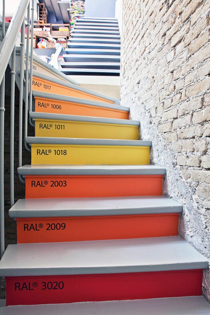 Winding staircase with risers in various RAL standard paint shades in staircase with exposed brick wall