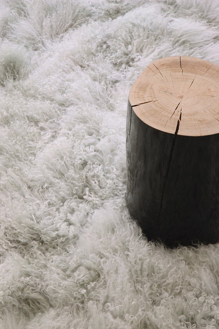 Side table made from black-painted tree stump on fluffy rug