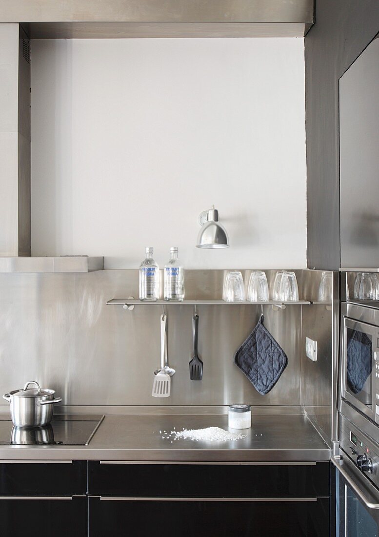 Detail of kitchen counter, bottles and glasses on shelf and wall-mounted lamp