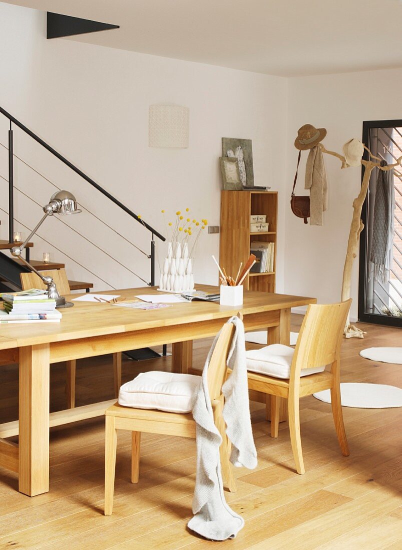 Writing utensils on wooden table and wooden chairs in front of slim balustrade on staircase and tree-shaped coat stand