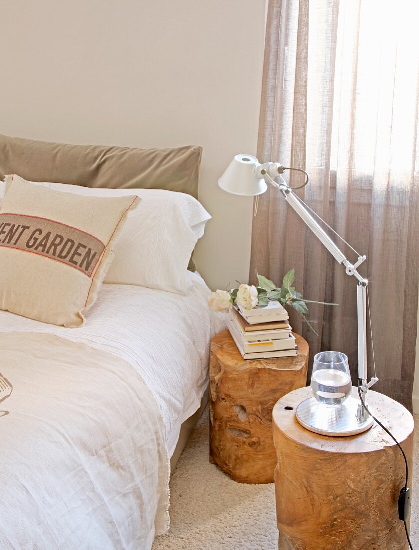 Stacked books and table lamp on tree-stump stools used as bedside tables next to double bed