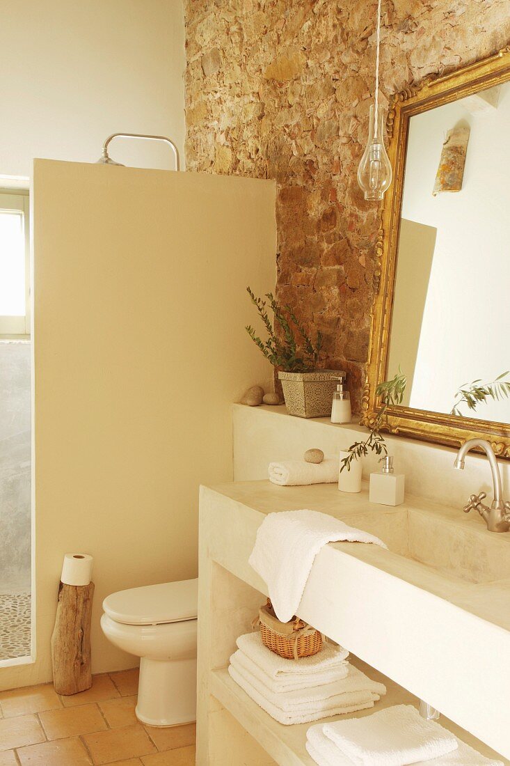 Exposed stone wall and masonry furnishings in rustic bathroom