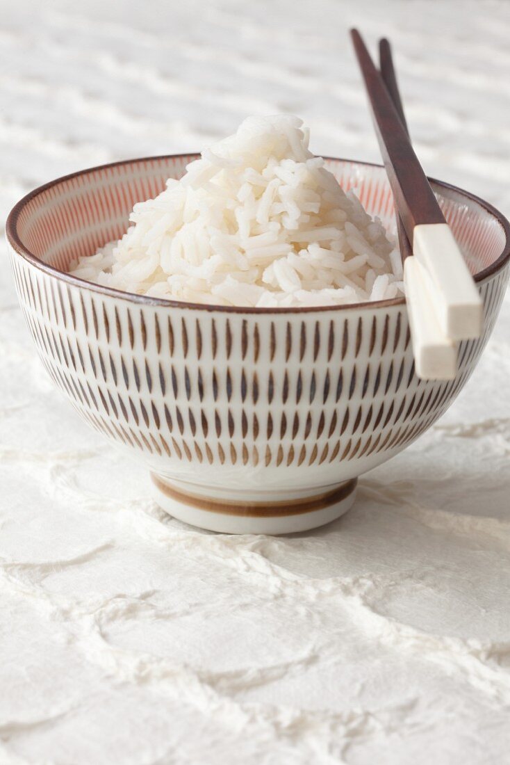 Boiled rice in a bowl with chopsticks