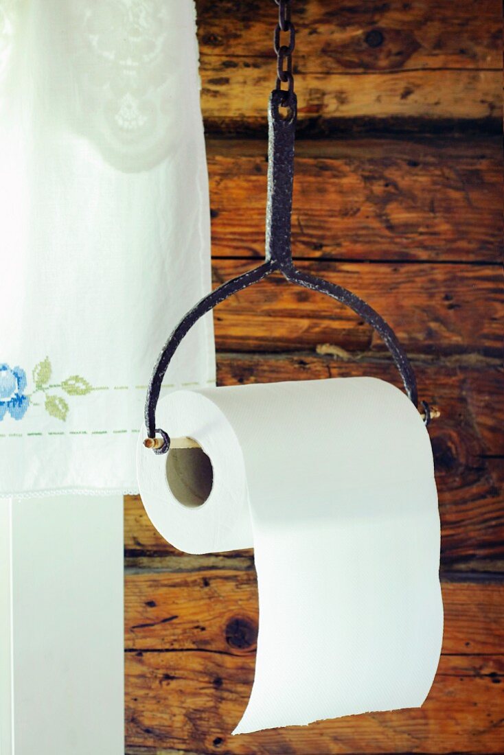 Toilet roll hung from old iron holder against rustic wooden wall