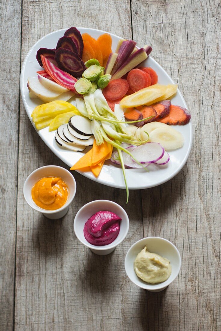 A plate of raw winter vegetables with three vegetable dips