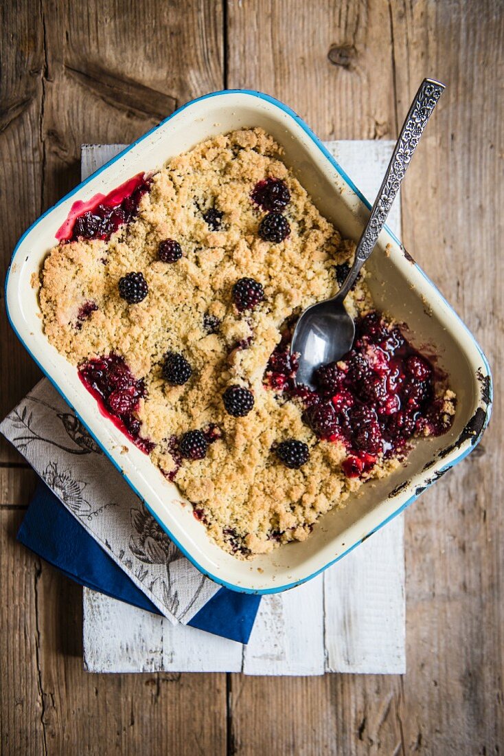 Blackberry & apple crumble in an enamel dish with a spoon (seen from above)