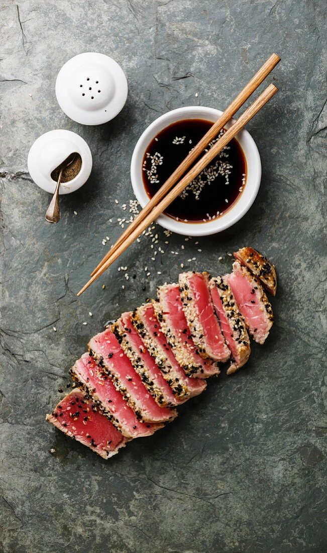 Sliced grilled Tuna steak in sesame and soy sauce on stone slate board