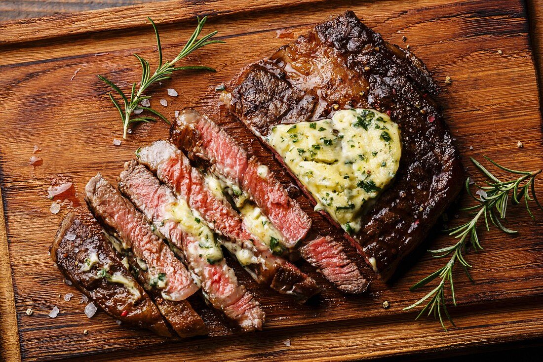 Sliced grilled Medium rare barbecue steak Ribeye with herb butter on cutting board