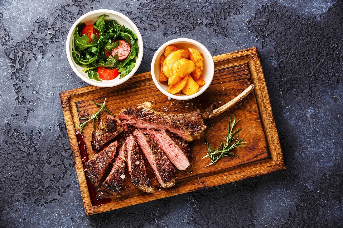 Sliced grilled Medium rare barbecue Steak on bone Veal rib with potato wedges and tomato and arugula salad
