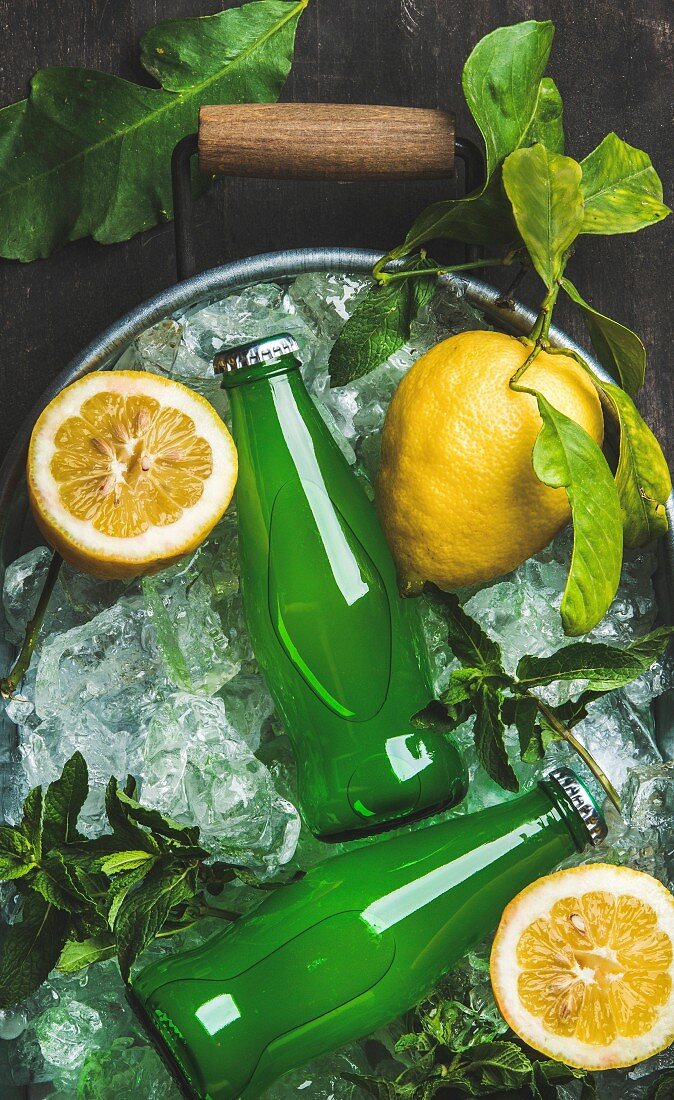 Bottles of green lemonade on chipped ice in metal tray with fresh lemons