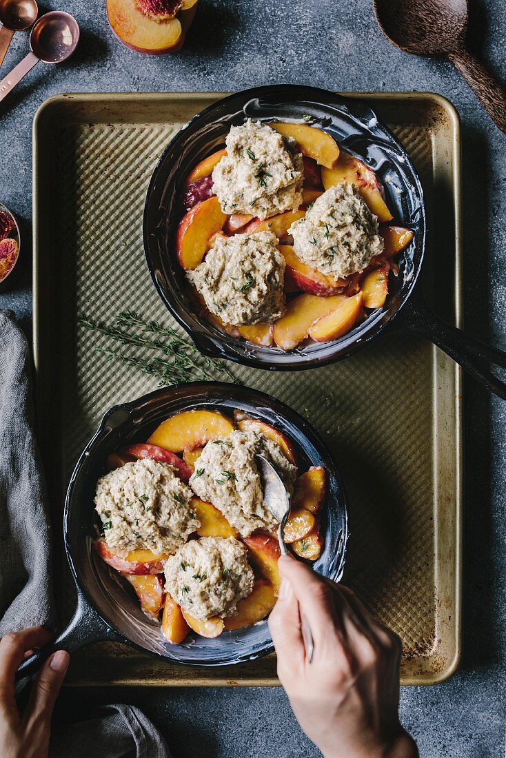 A woman is placing the last biscuit on top of peaches