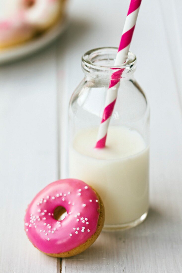 Doughnut mit pinkfarbener Glasur und eine Milchflasche mit Trinkhalm