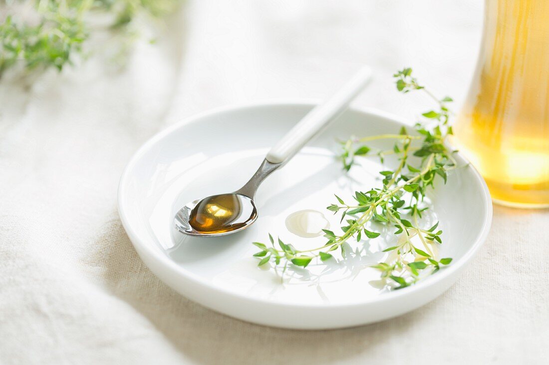 A spoon of home-made thyme syrup (used as cough medicine) on a spoon with a sprig of thyme