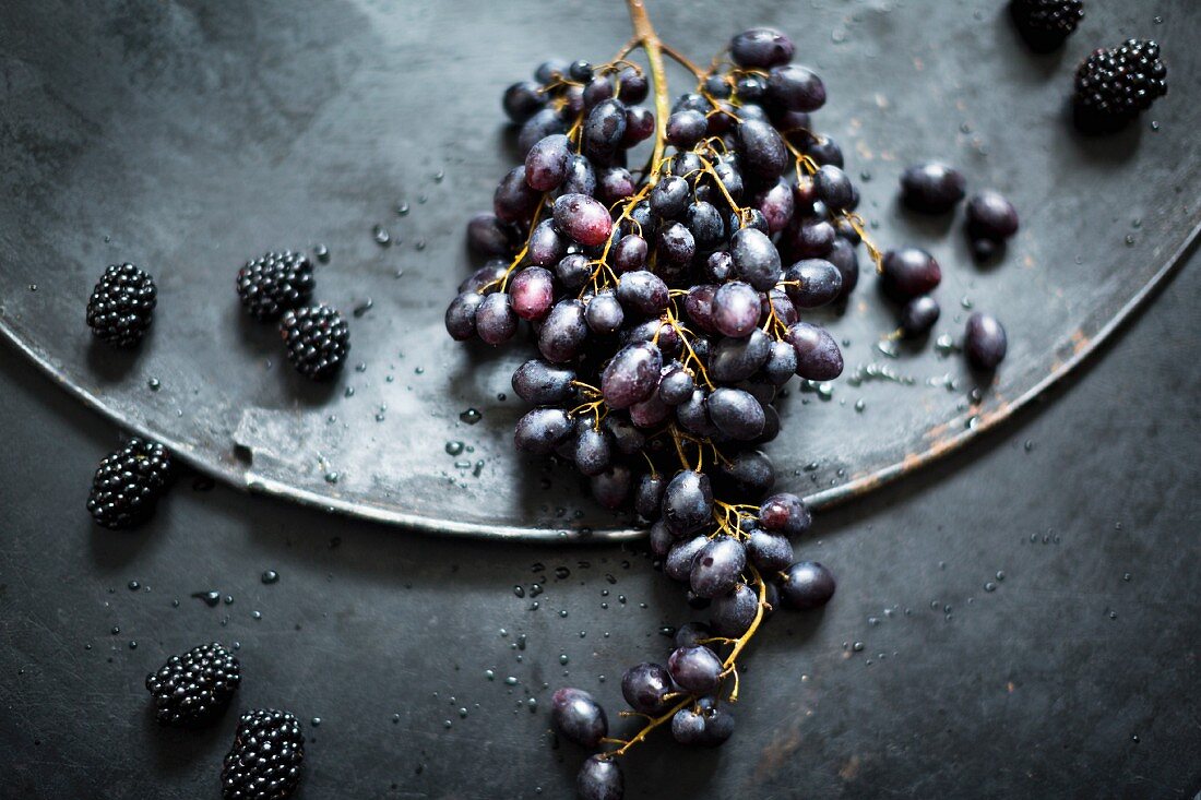 An arrangement with red grapes and blackberries on an old metal surface