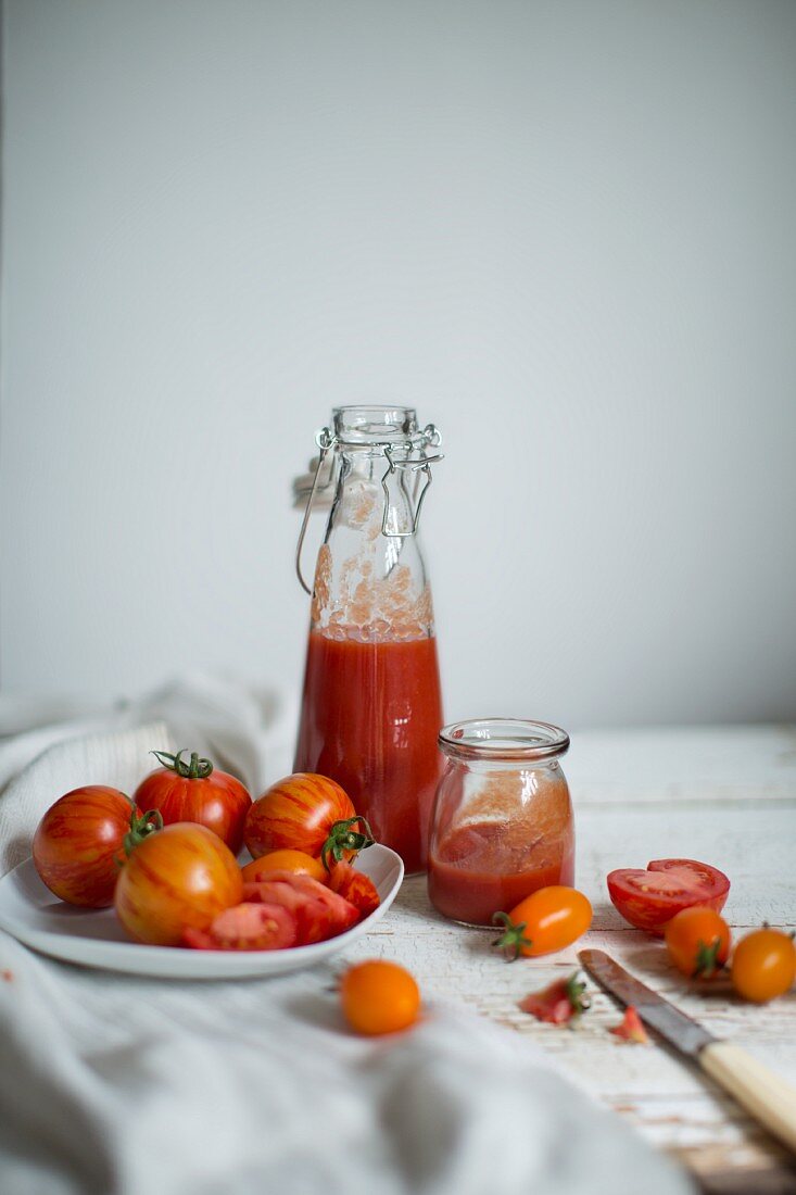 Stillleben mit Tomaten (Sorten: Red Zebra und Saint Orange) und frischem Tomatensaft in Gläsern auf altem Tuch